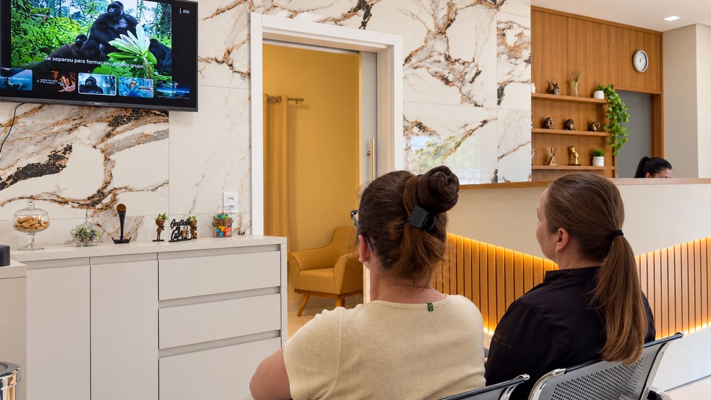 Pessoas aguardando atendimento na sala de espera da Clínica PsicoVivendo, com TV e recepção ao fundo